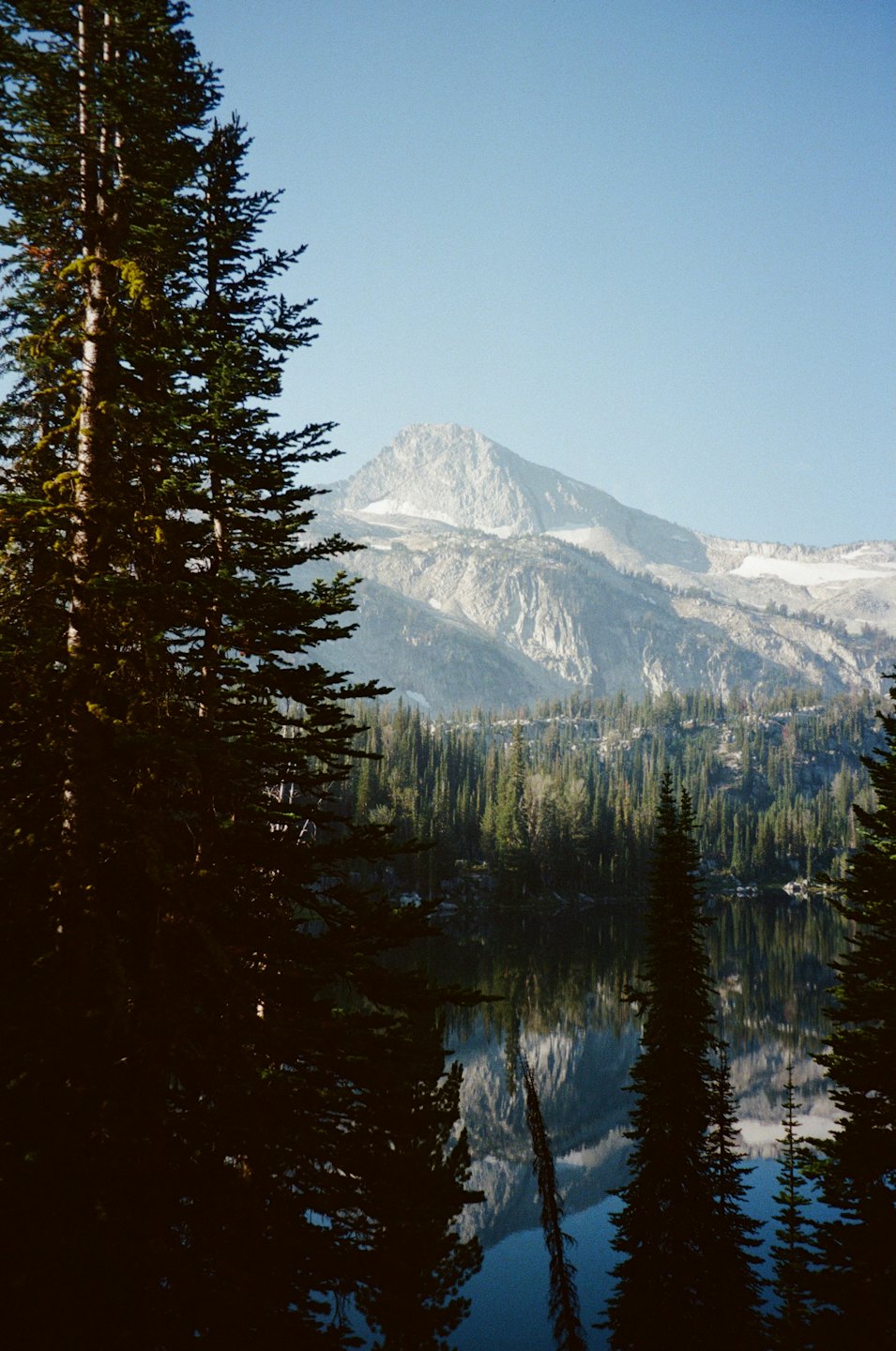 Snow-capped mountains and evergreen trees reflected in a still lake.