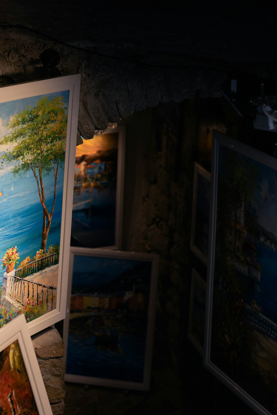 Framed coastal landscape paintings displayed against a stone wall.